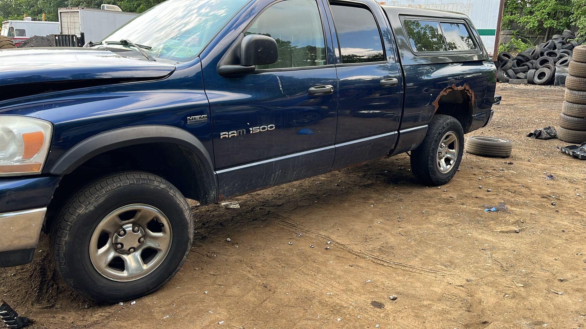 Older blue Dodge Ram 1500 pickup with visible rust damage parked at a recycling yard