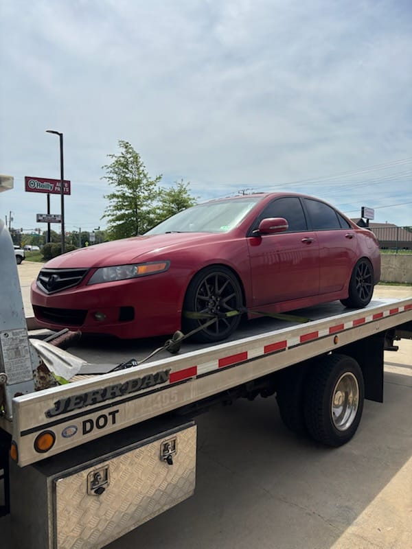 Red Acura sedan loaded onto a flatbed truck during a vehicle pickup in Leesburg, VA