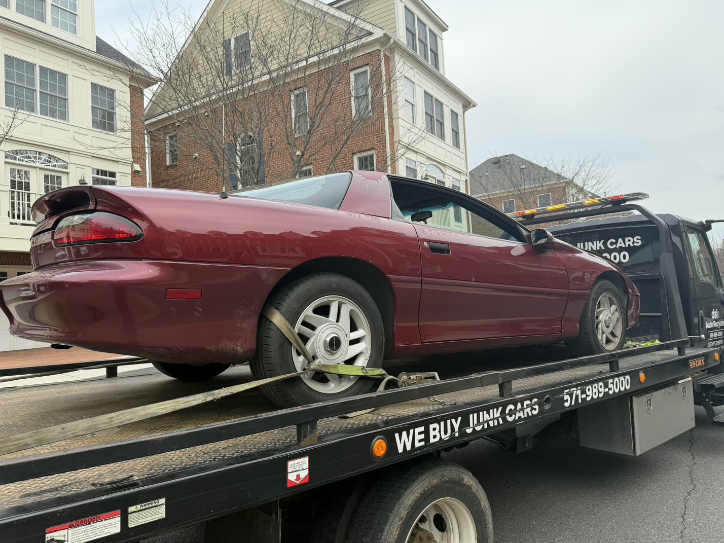 Older Camaro loaded onto a Dalo Auto Recycling flatbed truck in a Leesburg townhome community