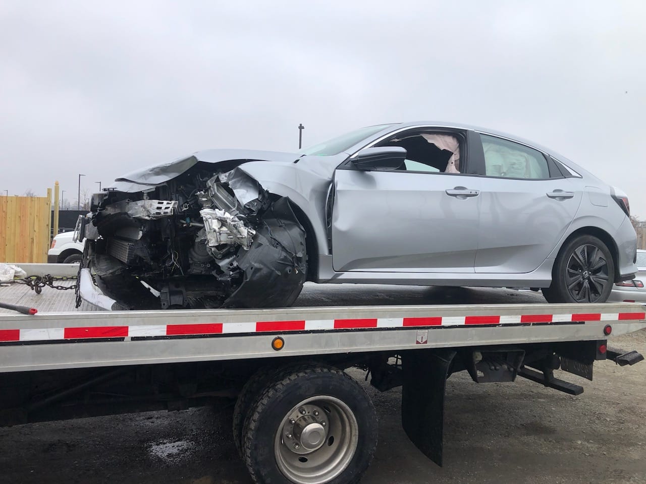 Wrecked silver Honda Civic loaded on a flatbed rollback after a sudden accident in Northern Virginia